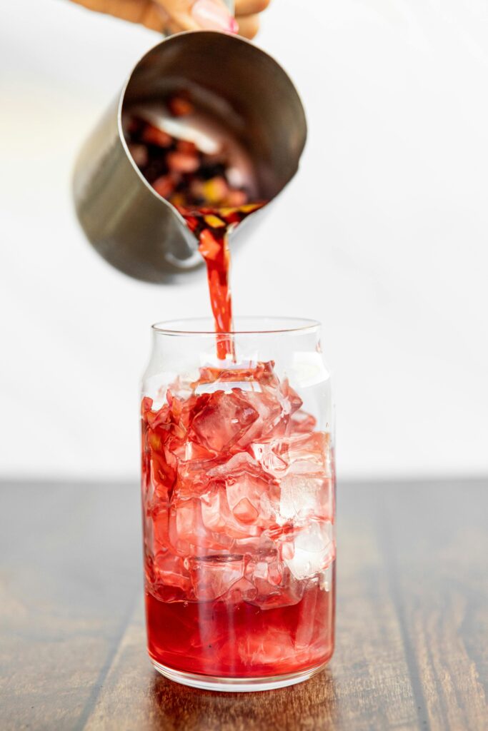 A tall glass of iced hibiscus tea garnished with lemon slices and fresh mint leaves, placed on a sunny outdoor table.