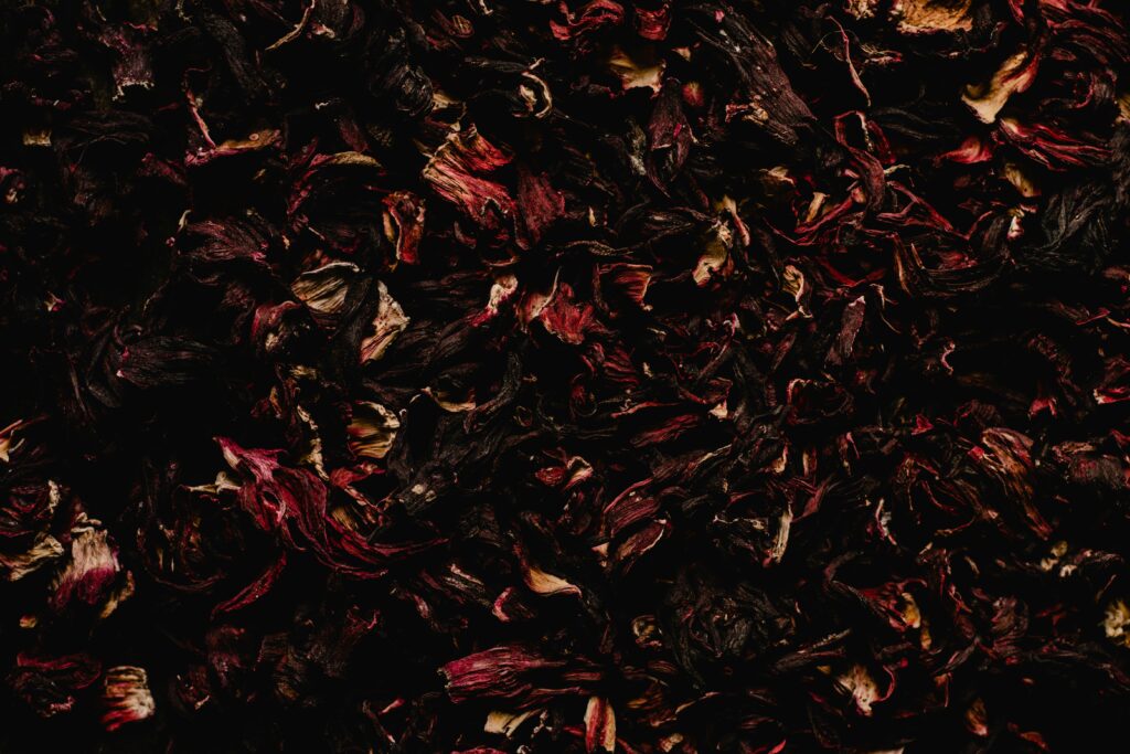 A rustic bowl filled with dried hibiscus petals next to a glass of freshly brewed hibiscus tea on a wooden table.