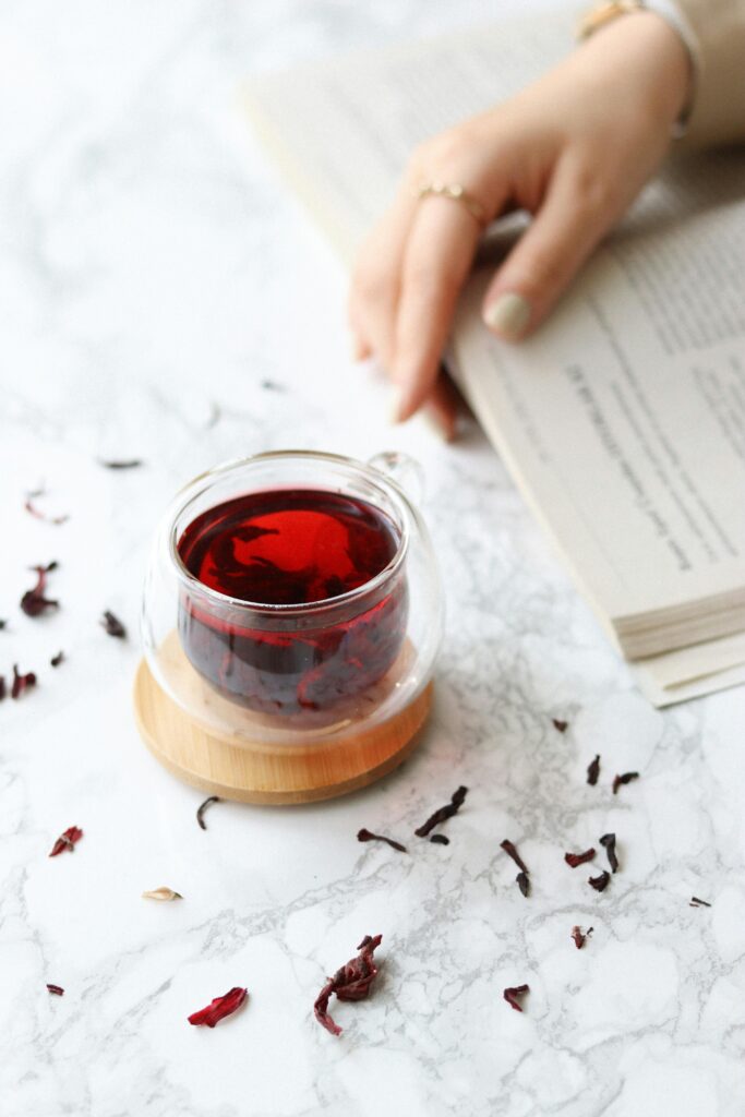 A warm cup of hibiscus tea placed on a bedside table with a dim lamp in the background, evoking a calming nighttime mood.