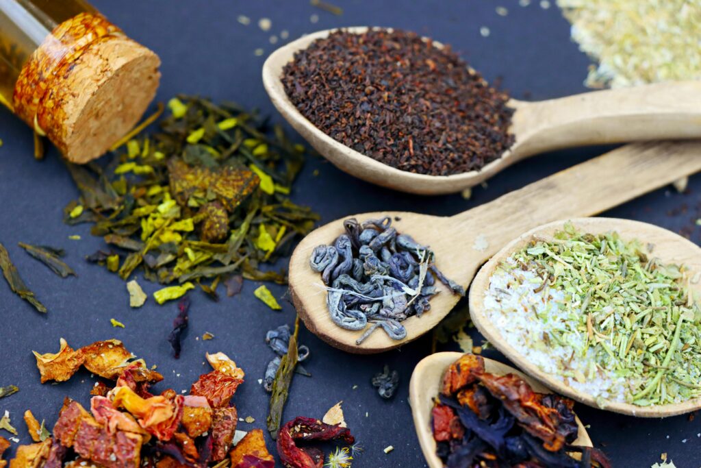 Assorted loose leaf herbal teas in wooden spoons on a flat lay composition, showcasing various colors and textures.