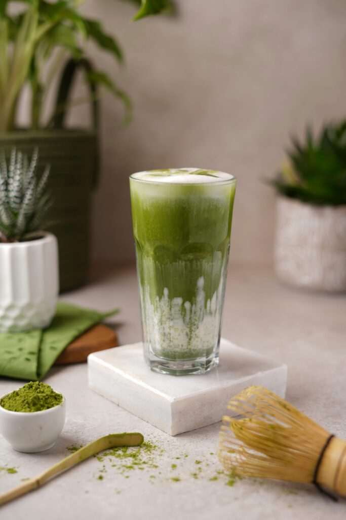 Green matcha latte in a tall glass with tools and plants, calm setting.