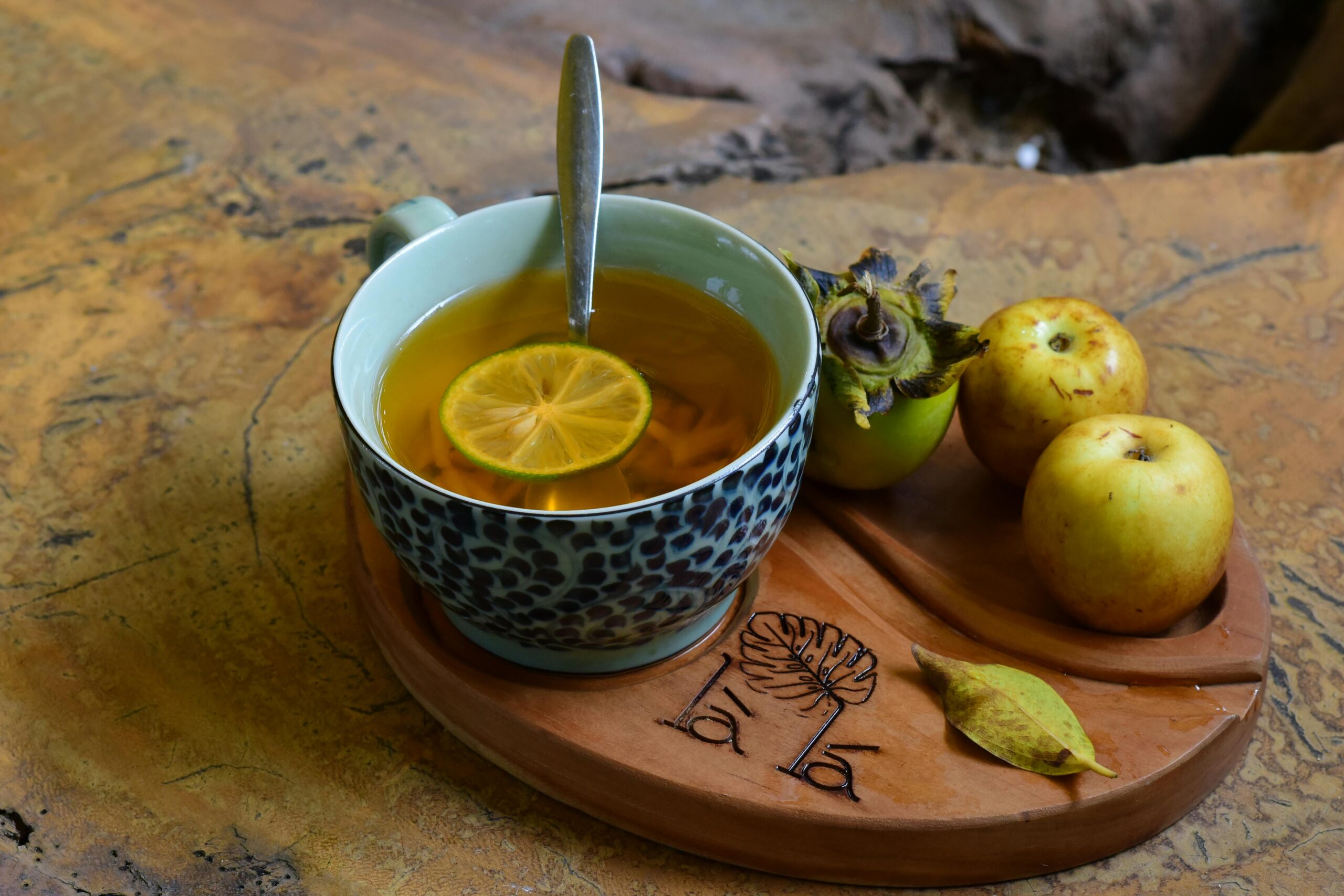 A warm cup of lemon tea with apples and persimmon on a decorative wooden tray, perfect for a cozy afternoon.