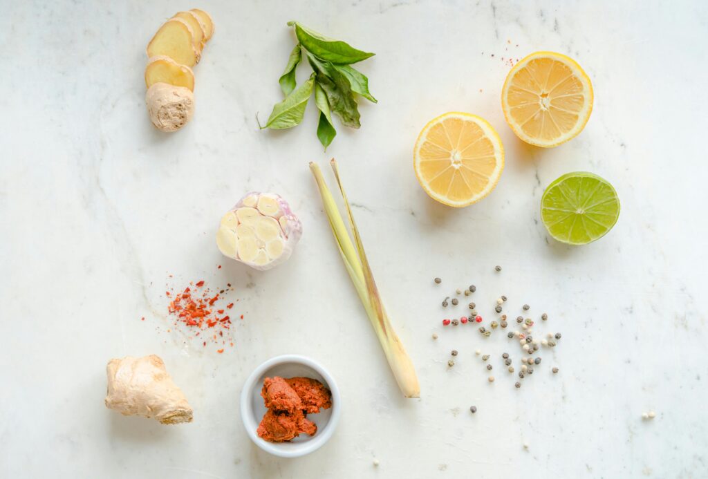 Top view of fresh ingredients including ginger, garlic, lemon, and spices on a white background.