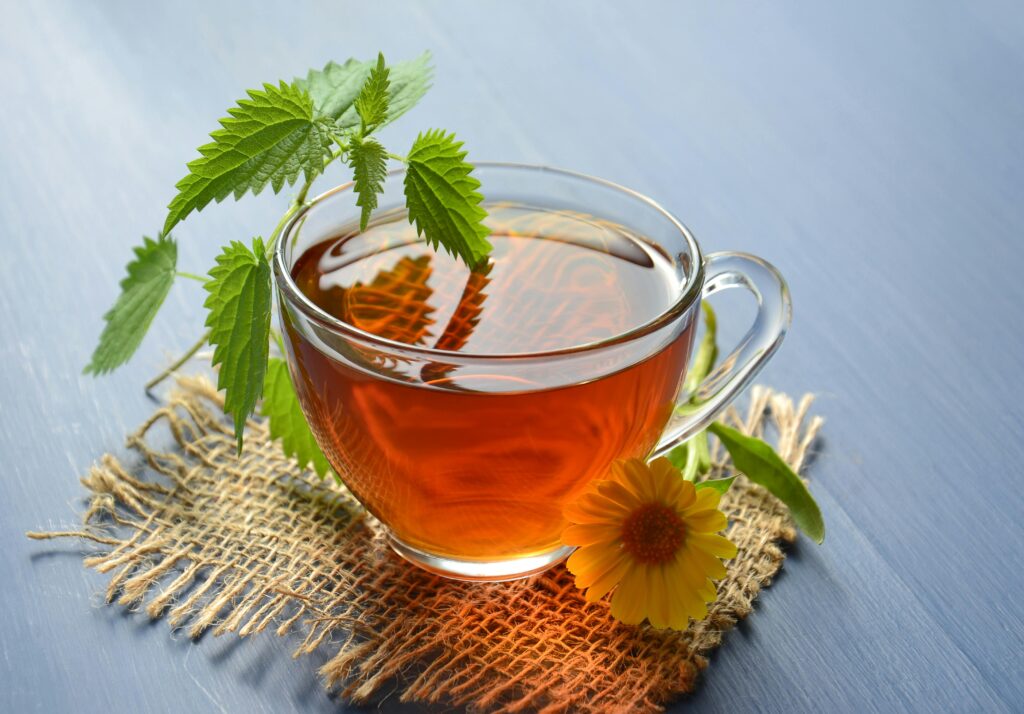 A refreshing glass cup of herbal tea garnished with nettle leaves and marigold flower.